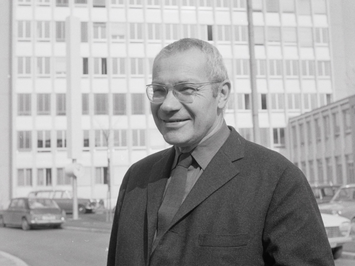 Max Bill in 1970, in a dark suit and glasses, in front of a building he designed in Zurich